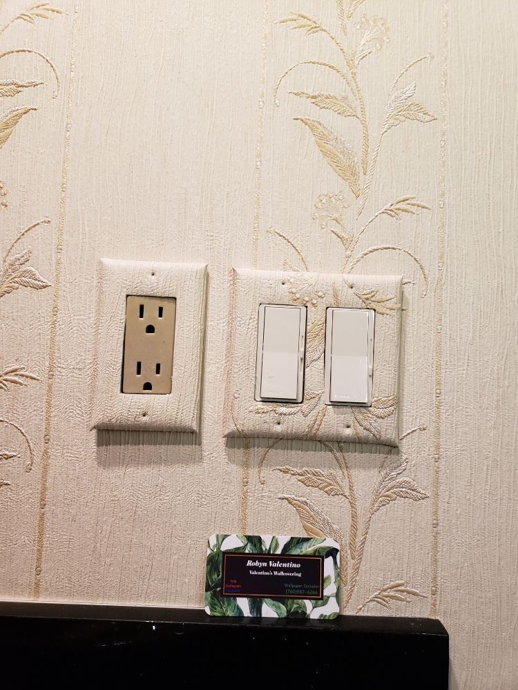 Close-up of textured wallpaper trimmed cleanly around a light switch and outlet