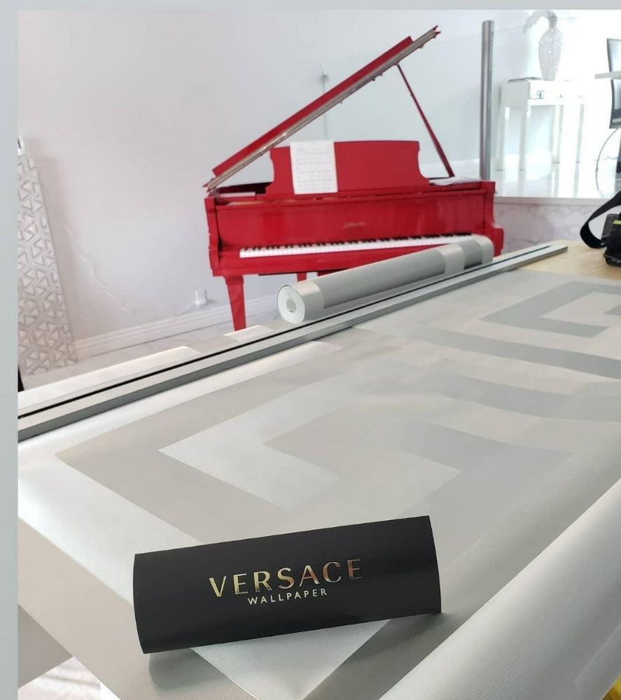 A roll of grey and white greek-key wallpaper unrolled on a work table in front of a red grand piano