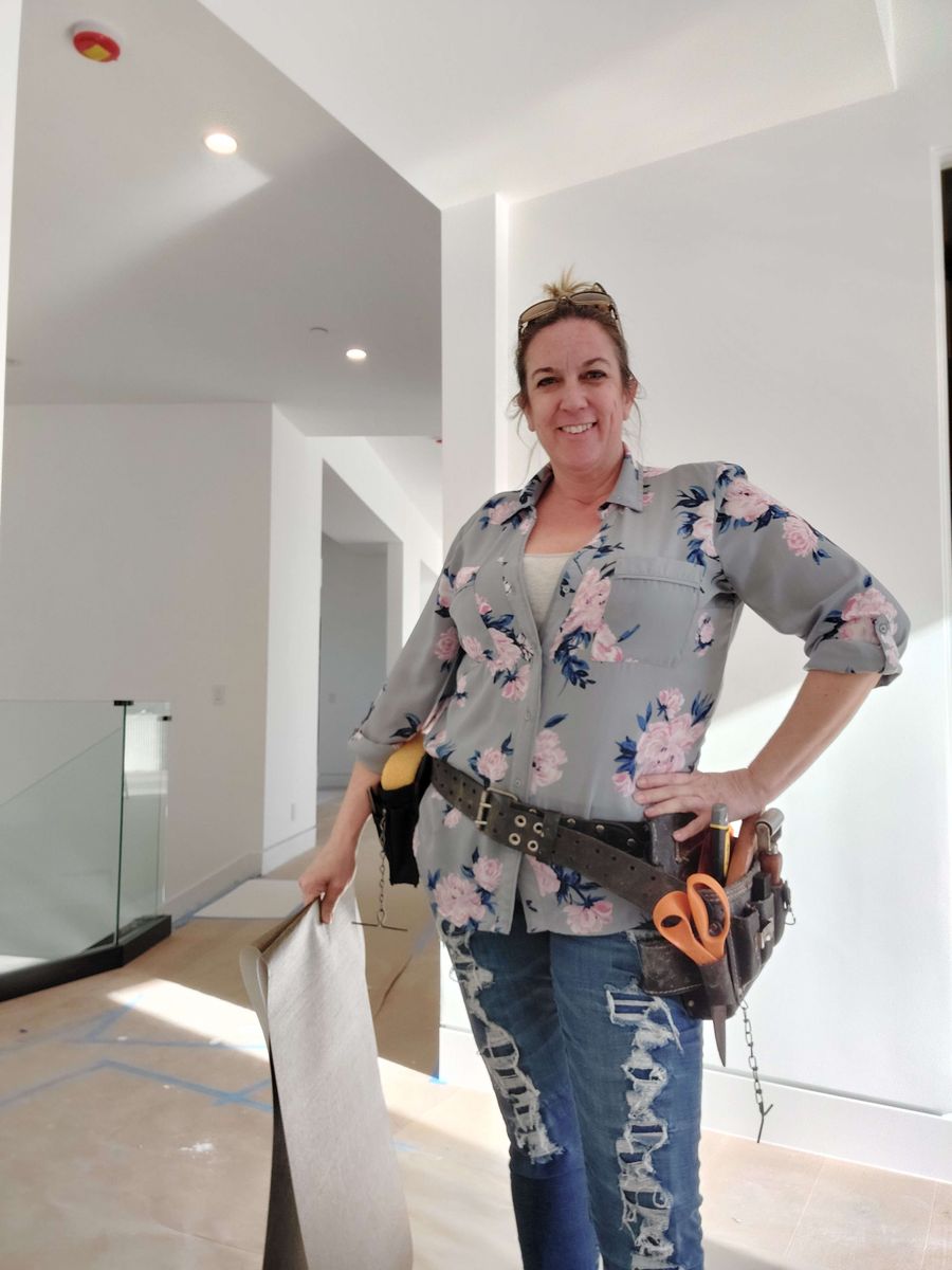Robyn Valentino on an install site, tool belt on, holding a roll of wallpaper