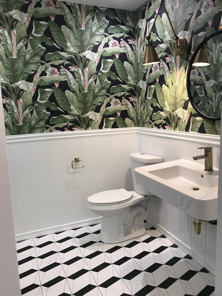 Powder room with green banana-leaf wallpaper above white wainscoting and a black-and-white geometric tile floor