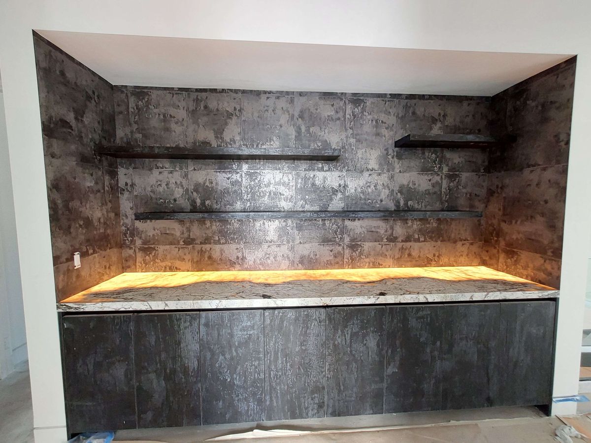 Bar niche with dark metallic textured wallcovering, lit floating shelves and a stone counter