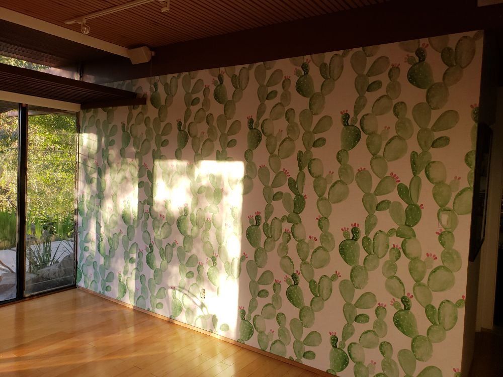 Sunlit accent wall with a green cactus-print wallpaper beside a sliding glass door