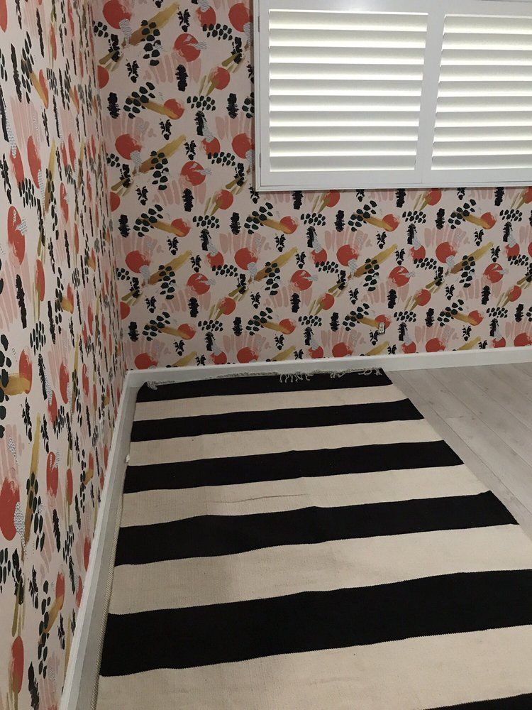 Room with coral and black floral wallpaper on every wall, white shutters and a black-and-white striped rug