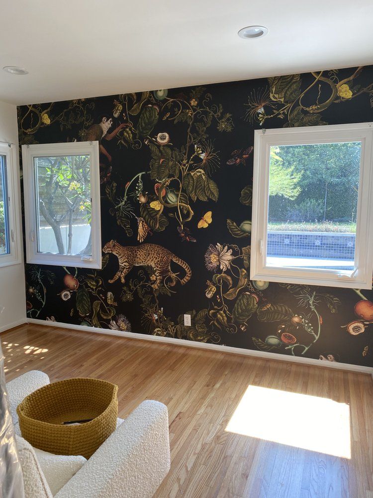 Bedroom with a dark green botanical mural of leaves and wildlife wrapping two walls around a window
