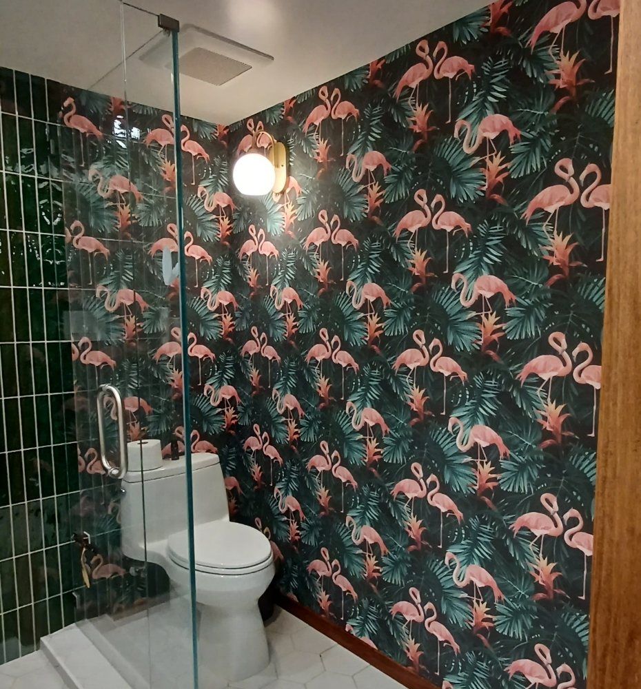 Bathroom with pink flamingo and palm wallpaper next to green subway tile and a glass shower