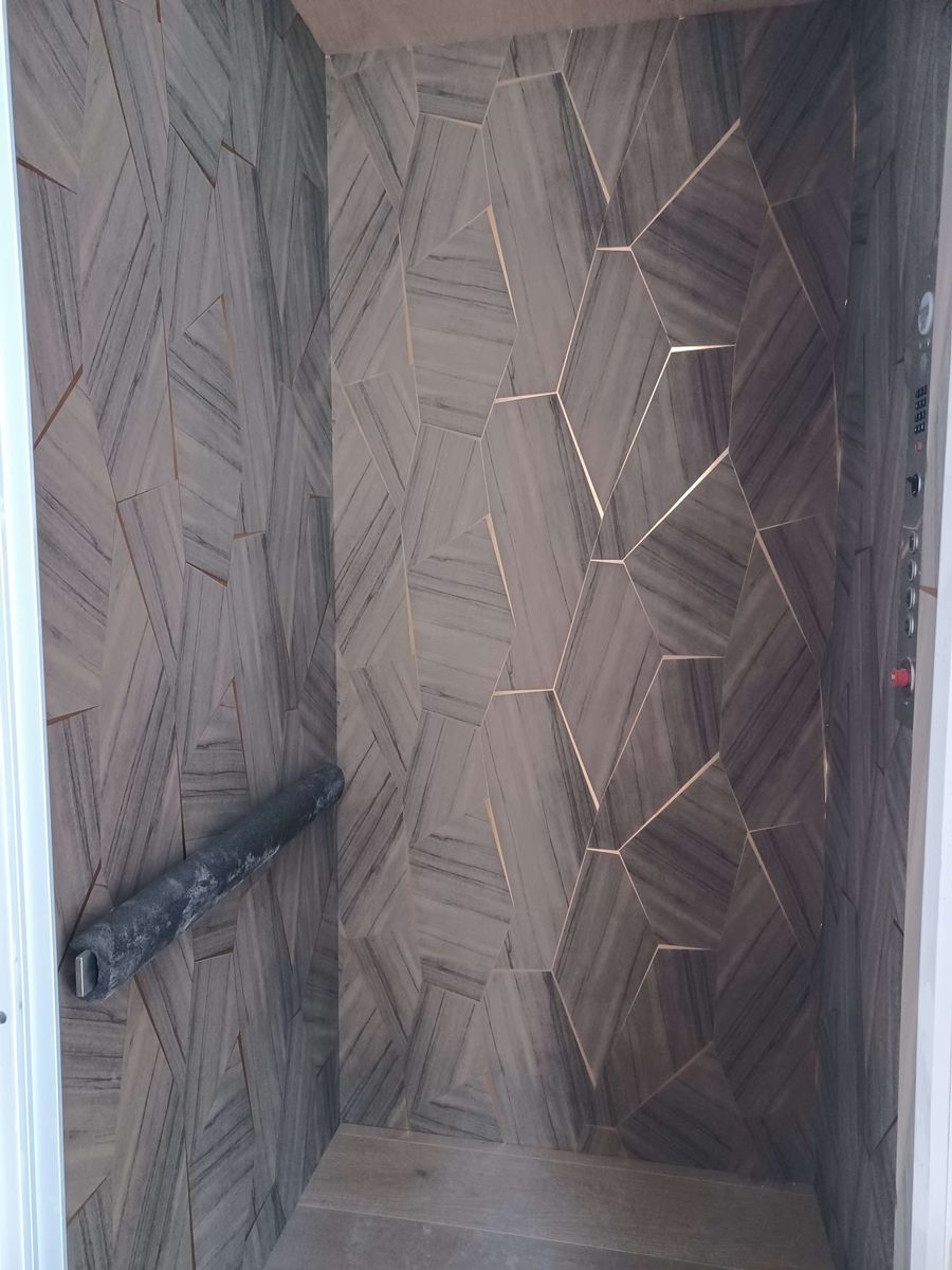 Feature wall of grey wood-grain geometric panels with thin brass inlay lines