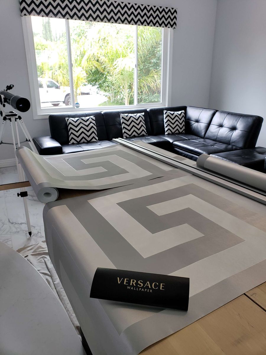 Grey and white greek-key wallpaper unrolled on a table in a living room before cutting