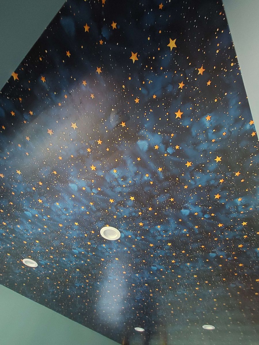 Ceiling covered in a night-sky mural of gold stars on deep blue with a recessed light