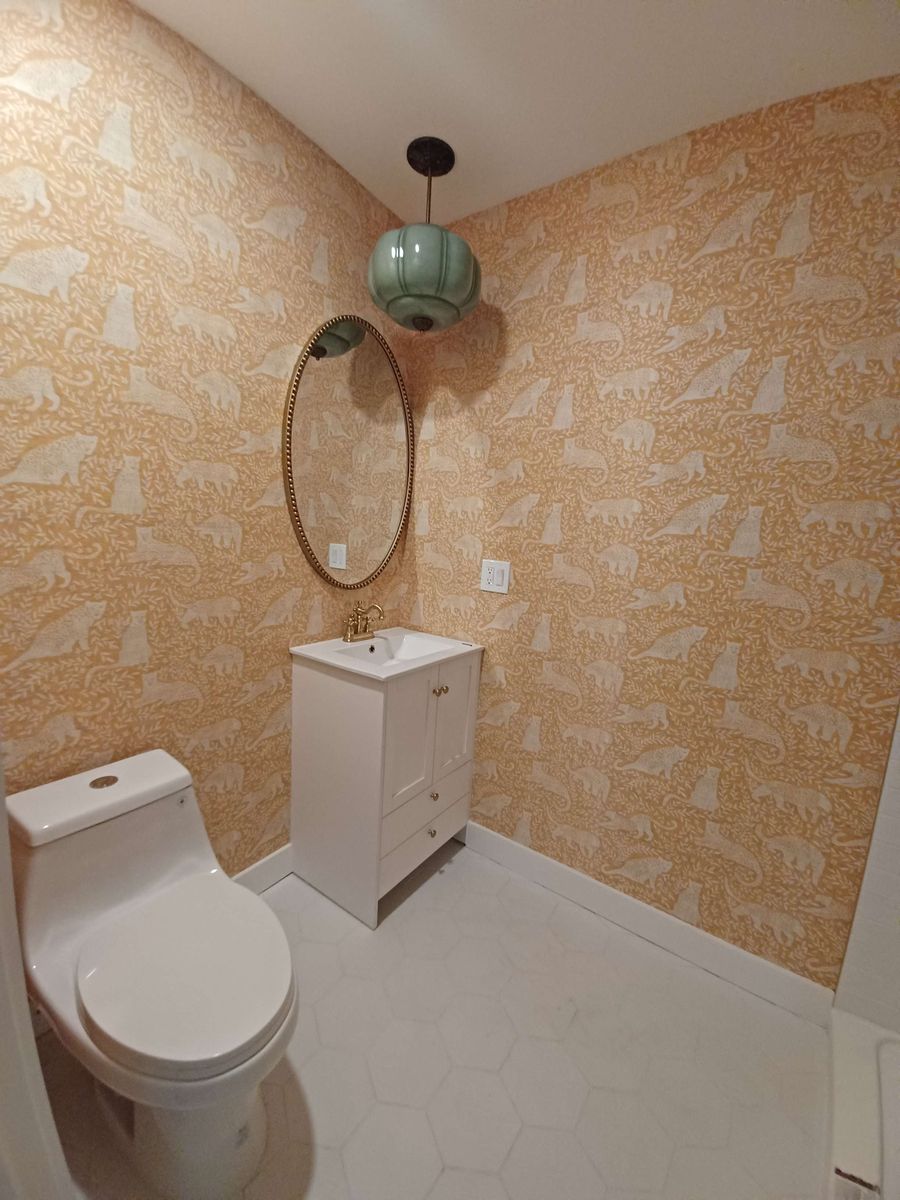 Powder bath with an ochre patterned wallpaper, a round brass mirror and a green glass pendant