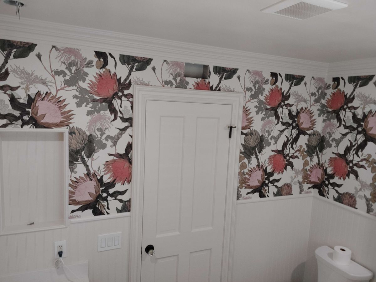 Hallway with large protea floral wallpaper above white wainscoting and a white door