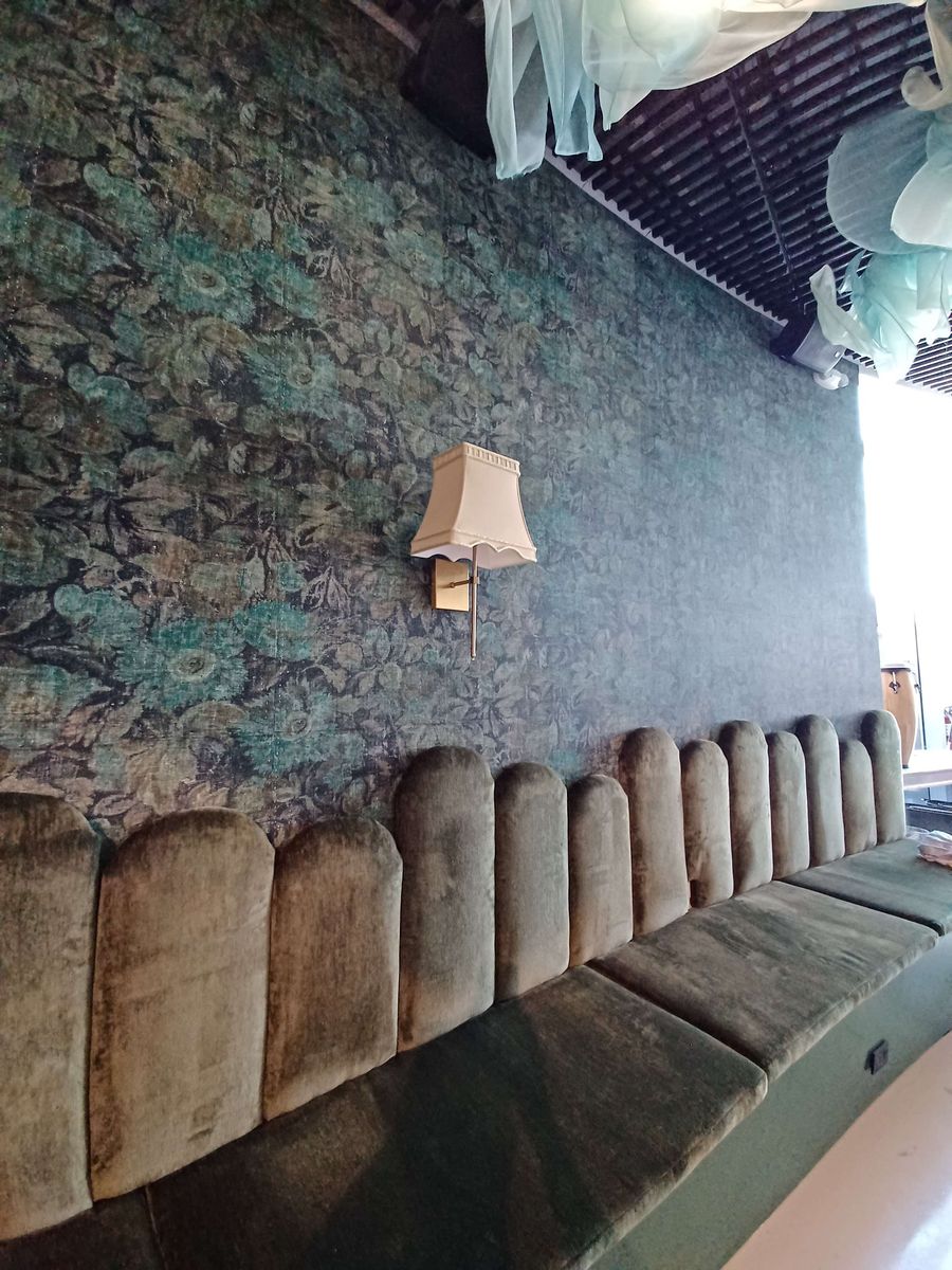 Bar wall with a teal vintage floral wallpaper, a shaded brass sconce and a scalloped green velvet banquette